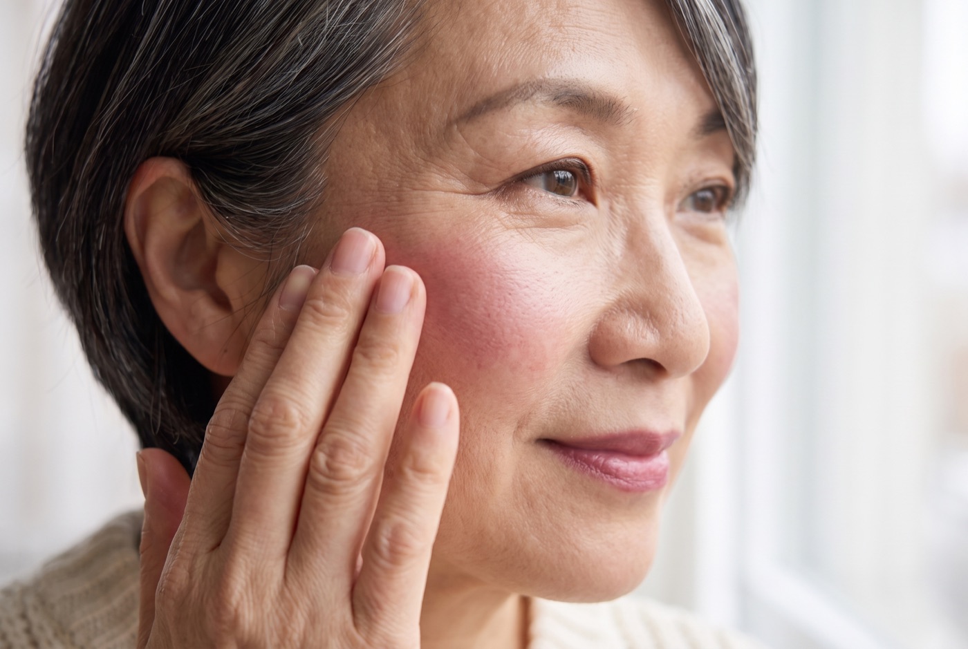 Two fingertips pressing berry cream blush high on the cheekbone toward the temple