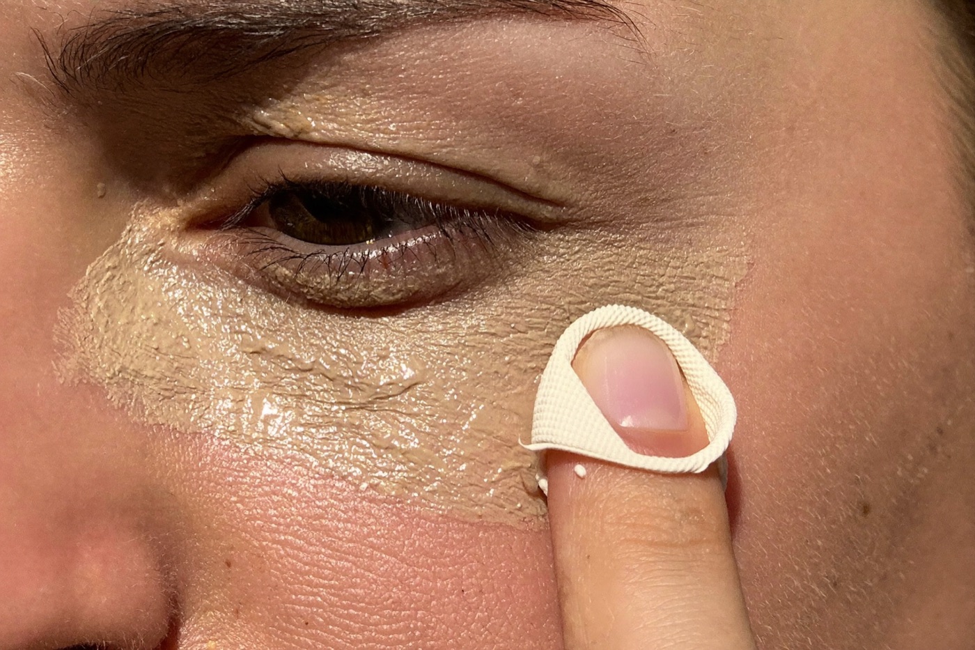 Close-up of concealer being applied in a triangle under the eye, blended with a fingertip in daylight