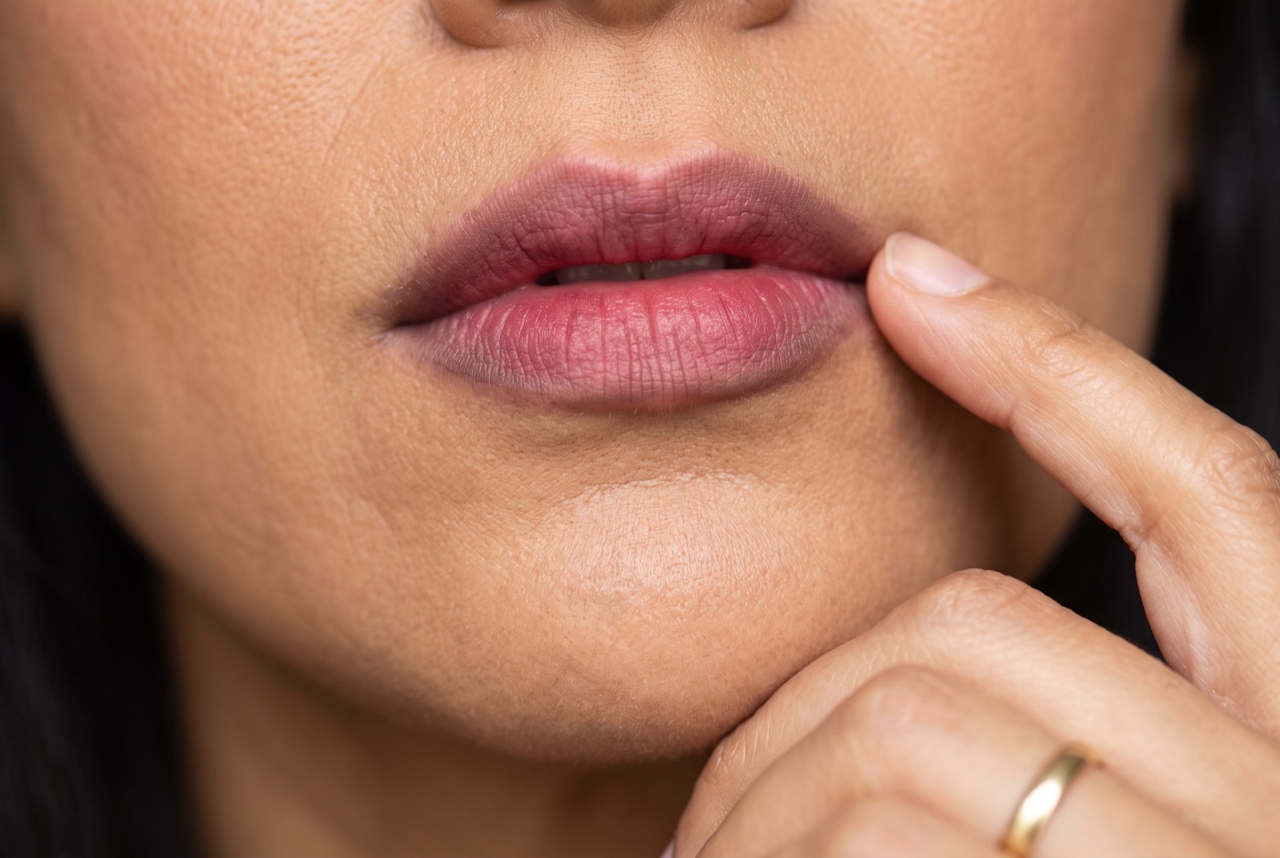 Close-up of berry-toned blurred lips with softly diffused edges and a fingertip tapping one corner of the mouth