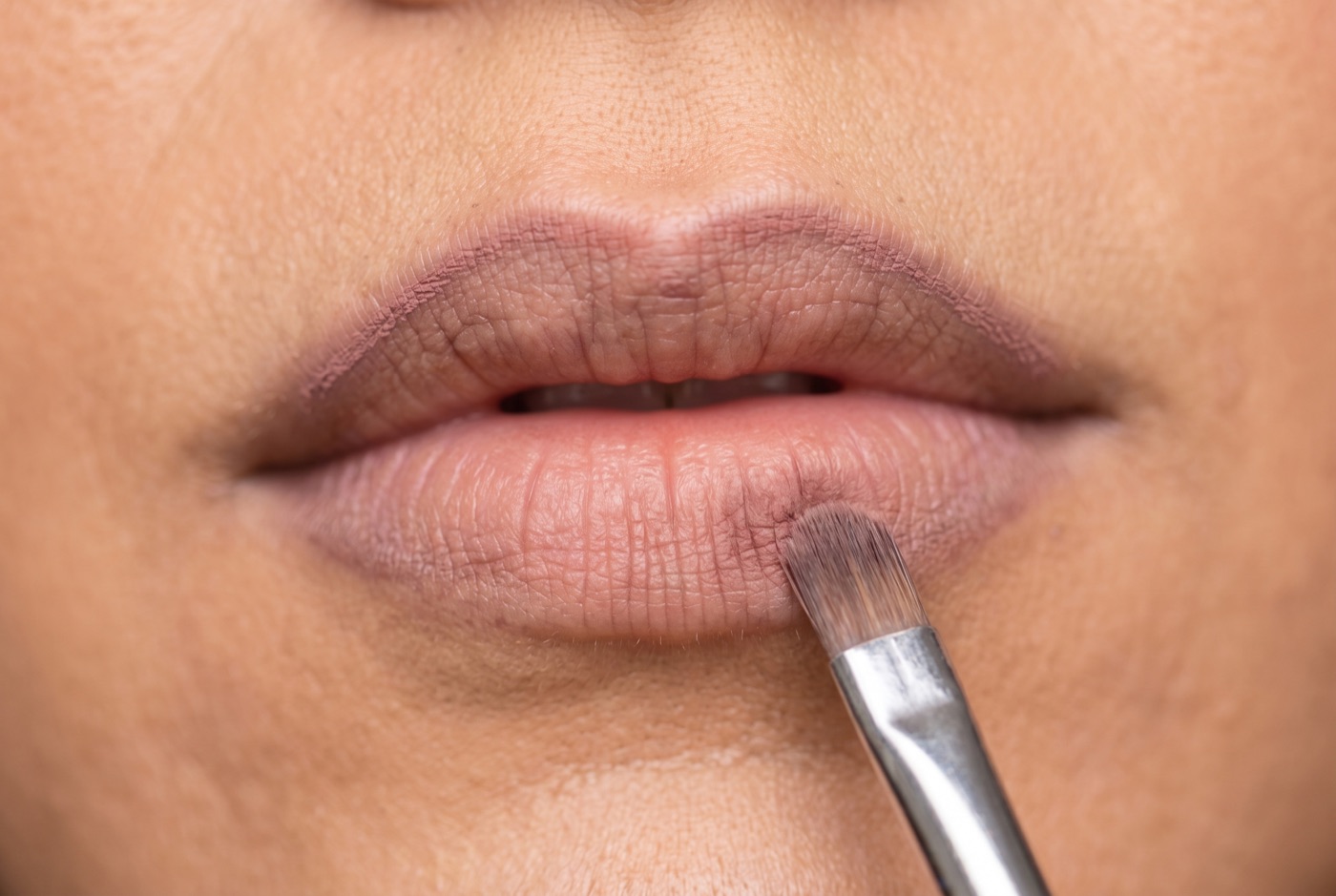 Soft mauve-brown lip liner kept just inside the lip line while a small brush blurs it inward on the lower lip