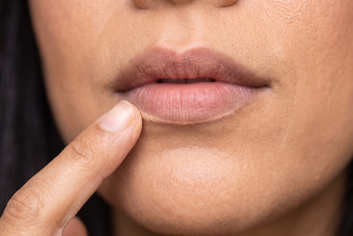 A ring fingertip tapping concealer around the edge of bare lips to soften the natural lip line