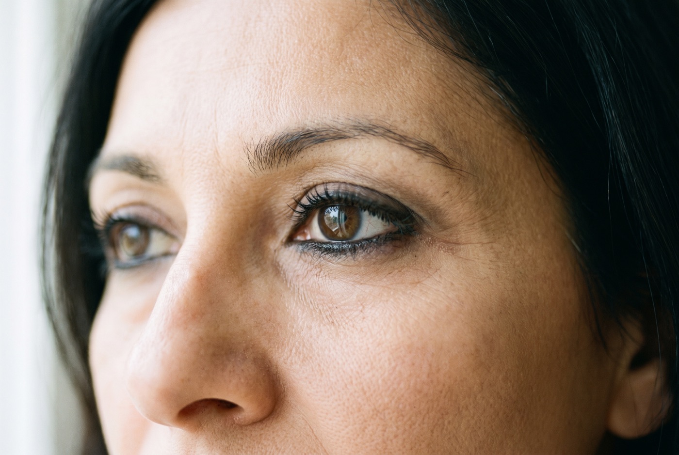 Soft black kohl eyeliner smudged along the upper and lower lash line of a woman in her forties, bare skin around the eye