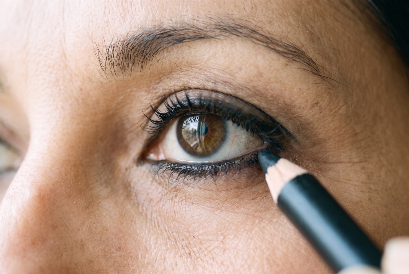 A kohl pencil pressing into the outer two-thirds of the lower lash line while the inner corner stays bare
