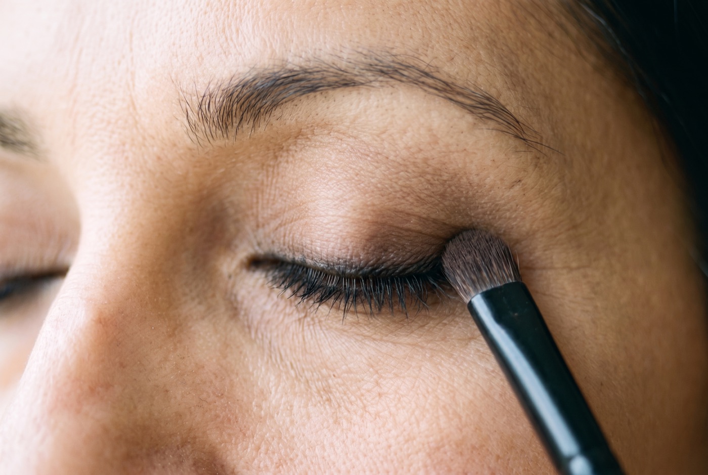 A smudge brush pressing dark brown eyeshadow over smudged kohl liner on a closed eye