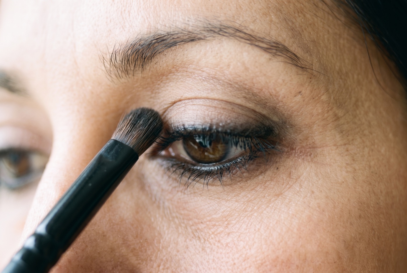 A small dense smudge brush flicking black kohl upward from the upper lash line into a soft haze