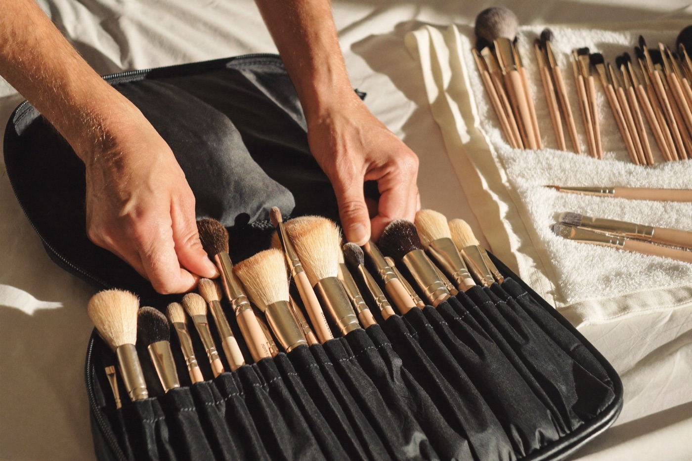 Two hands lifting a large handful of brushes out of an open kit bag