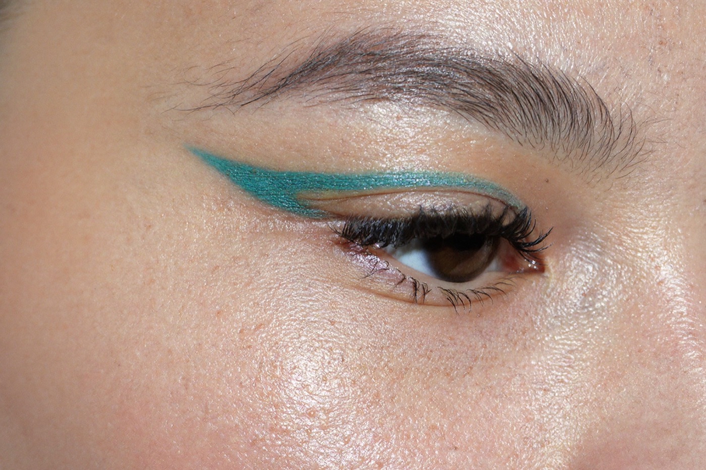 Close-up of a teal liner drawn along the upper lash line with an otherwise bare, glowing eye