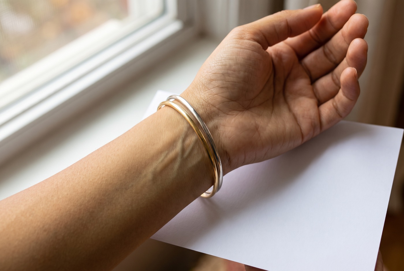 Inner wrist in window daylight with faint blue-green veins, wearing a gold and a silver bangle side by side